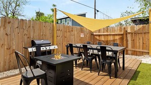 Una terraza de madera con una parrilla, mesa y sillas, una sombrilla amarilla y una cerca de madera.