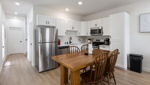 Una cocina moderna con armarios blancos, electrodomésticos de acero inoxidable y una mesa de comedor de madera.