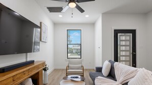 Una sala moderna con un televisor de pantalla plana, un mueble de madera para entretenimiento, un sofá gris y un ventilador de techo.