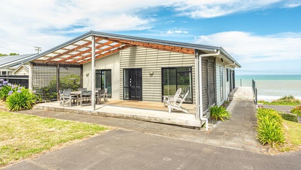 A coastal house with a covered patio, a dining area, and a view of the ocean. - Sunset Escape - Stunning Beachfront Views (Kai Iwi)