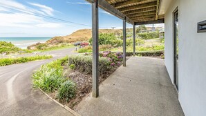 A covered outdoor area with a concrete pathway, wooden beams, and a view of the ocean. - Sunset Escape - Stunning Beachfront Views (Kai Iwi)