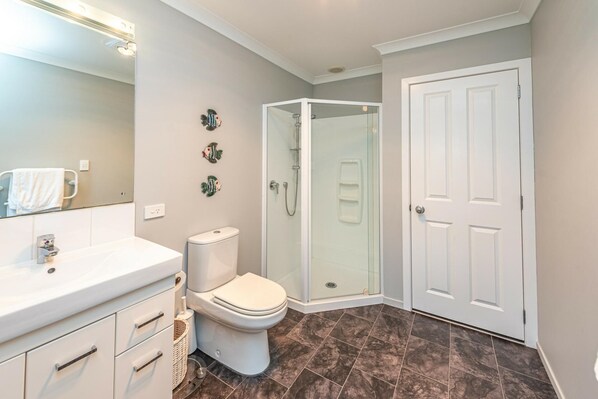 Een badkamer met een wit toilet, een douchecabine van glas, een witte wastafel en een witte deur.