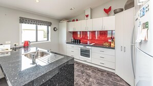 A modern kitchen with white cabinets, a granite countertop, a built-in oven, and a refrigerator. - Sunset Escape - Stunning Beachfront Views (Kai Iwi)