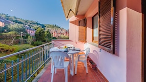 Varanda com mesa e cadeiras, com vista para uma colina com edifícios.