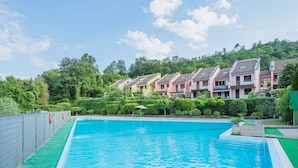 Piscina com deck verde, rodeada por uma cerca. Ao fundo, edifícios altos com varandas.