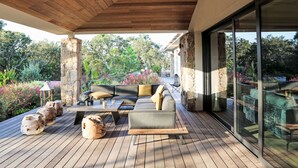 A covered outdoor seating area with a wooden deck, stone pillars, and a view of a garden with various plants and flowers. - La Cupulatta by Interhome (Sainte Lucie Porto Vecchio)