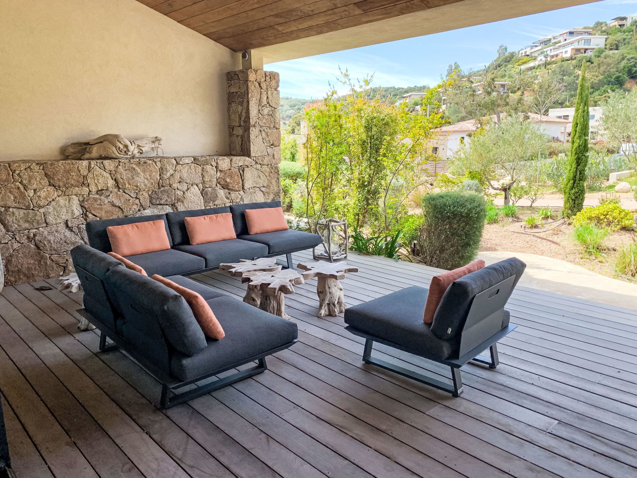 Zona relax all'aperto con muretto in pietra, terrazza in legno e vista su una collina con case.