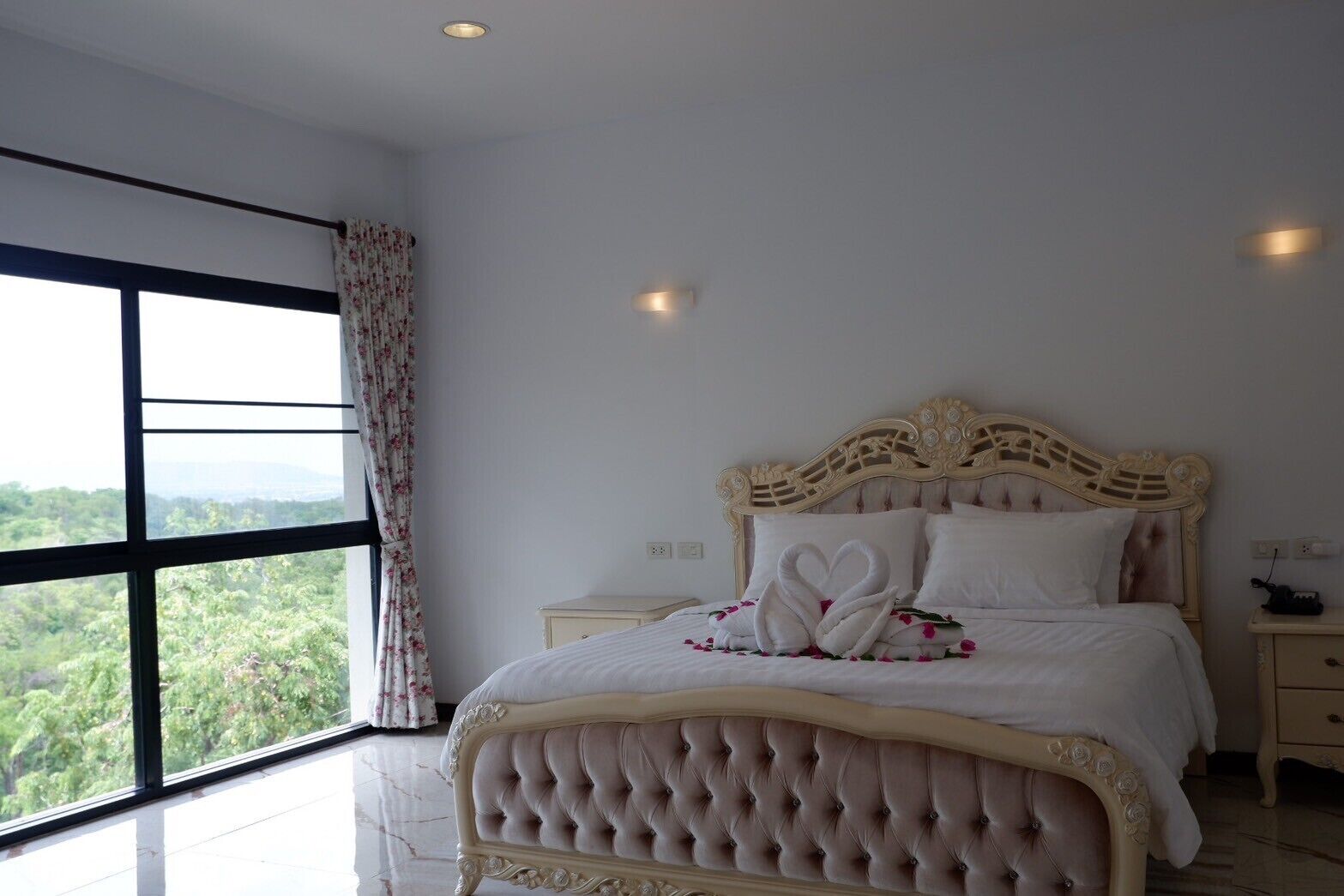 A large bed with a tufted headboard, a nightstand, and a window with curtains.