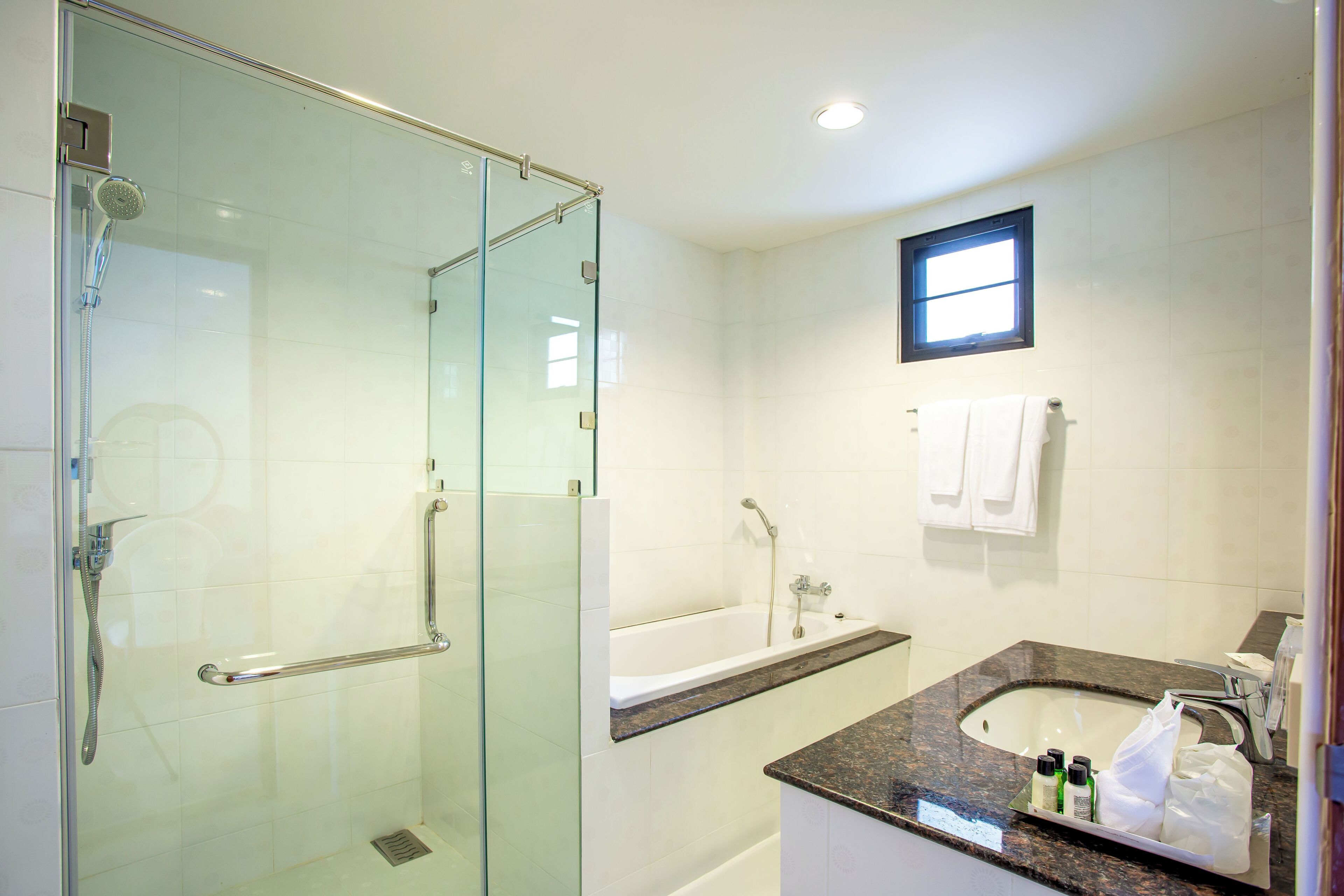 Un baño moderno con ducha de vidrio, bañera y lavamanos de encimera de granito.