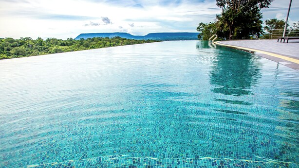 A clear blue infinity pool with a view of a lush green landscape and distant mountains. - Channgarm Mountain View Resort  (Sikhio)