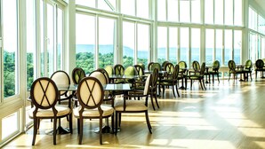 A spacious dining area with multiple tables and chairs, large windows offering a view of greenery and mountains. - Channgarm Mountain View Resort  (Sikhio)