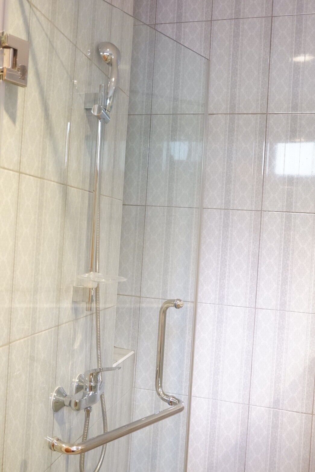 A shower area with a handheld showerhead, a handheld shower attachment, and a grab bar.