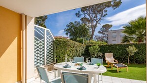 A patio with a round table and chairs, a glass door, and a view of a garden and building. - Le Clos Saint Saens by Interhome (Saint Aygulf)