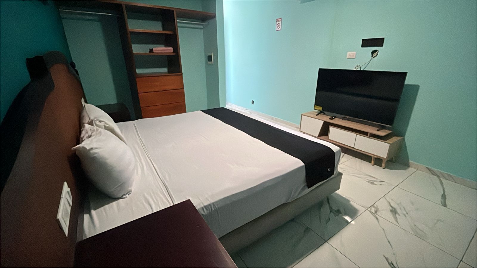 Un dormitorio con cama, televisión sobre un mueble, armario y puerta.