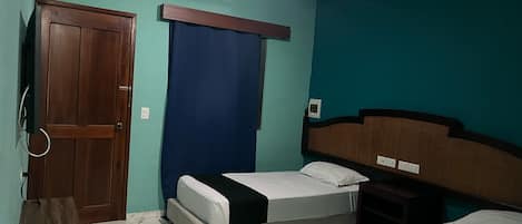 Una habitación con dos camas, un ventilador de techo, una puerta de madera y una cortina azul.