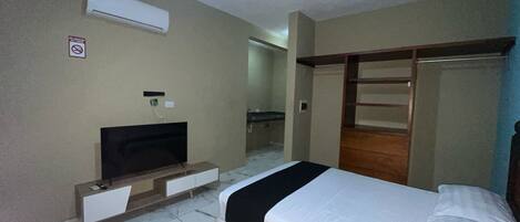 A hotel room with two beds, a TV, a wardrobe, and a bathroom visible in the background.