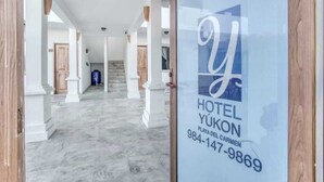 A hotel entrance with a marble floor, white pillars, and a glass door displaying the hotel's name and contact number. - Hotel Yukon (Playa del Carmen)