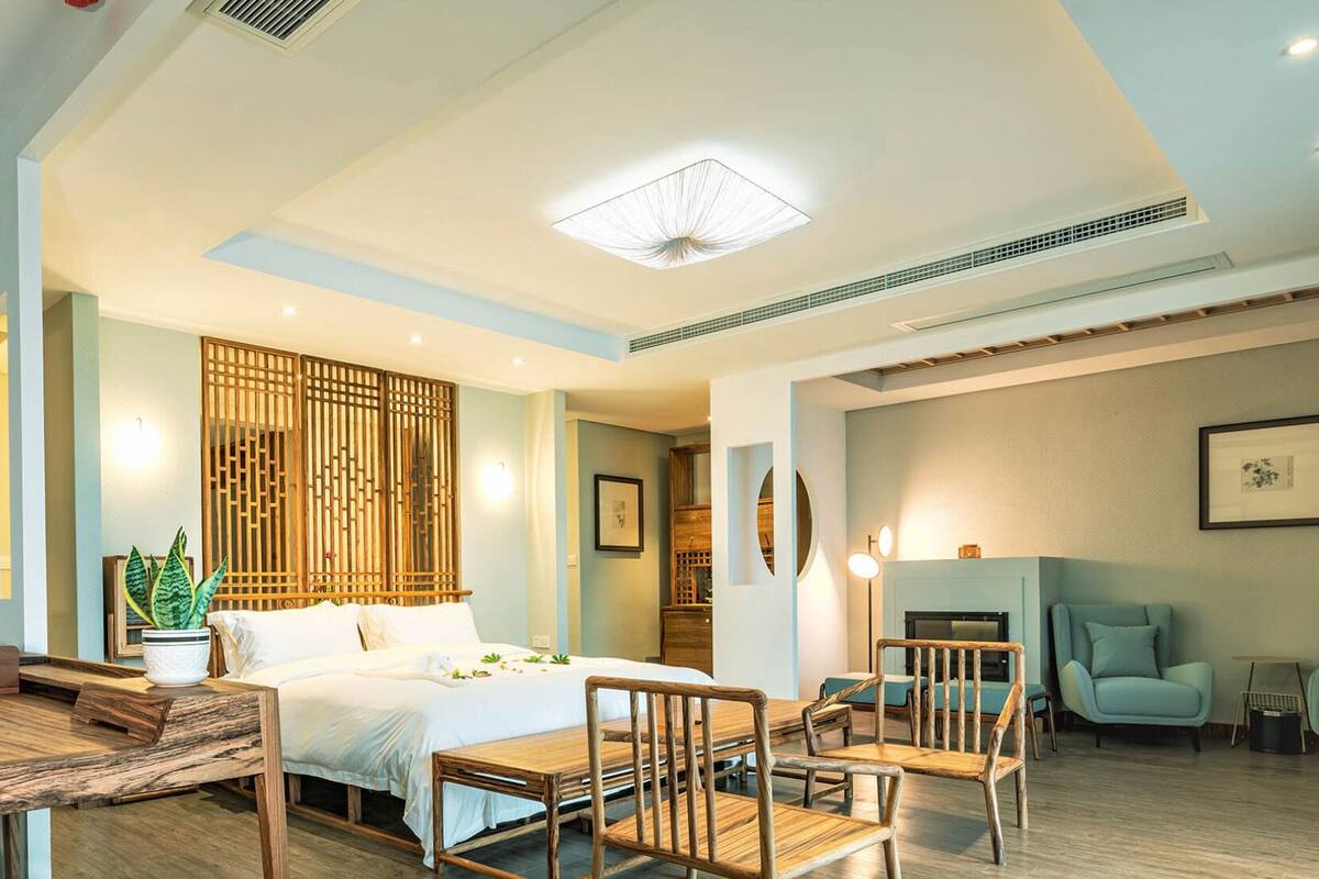 A modern hotel room with a bed, wooden furniture, a dining area, and a staircase.