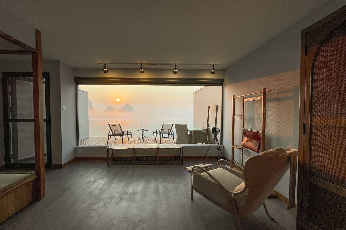 A modern room with a large window overlooking a scenic view, a wooden floor, and a seating area with chairs and a table.