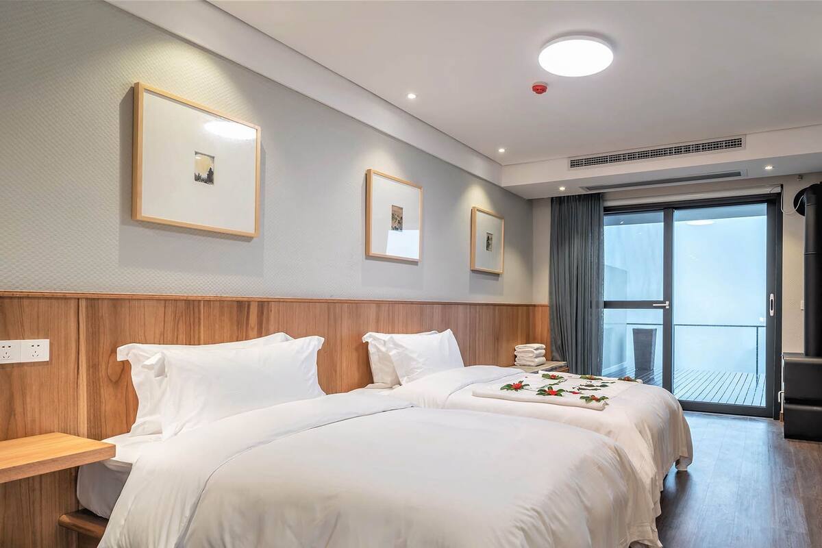 A hotel room with two beds, a large window, a flat-screen TV, and framed pictures on the wall.