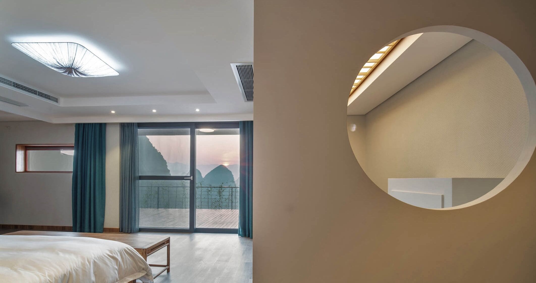 Une chambre d’hôtel moderne avec un grand lit, une vue sur les montagnes depuis le balcon et une étagère circulaire fixée au mur.