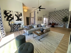 Ein modernes Wohnzimmer mit einer Couch, einem Couchtisch, Poufs und Kunstwerken an den Wänden.