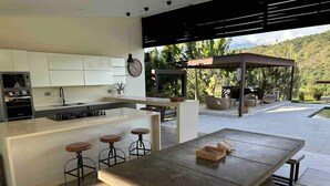 Una cocina moderna con armarios blancos, una isla central con taburetes y una zona de comedor con una mesa grande y bancos.