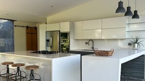 Una cocina moderna con una isla central, taburetes de bar, electrodomésticos de acero inoxidable e iluminación colgante.