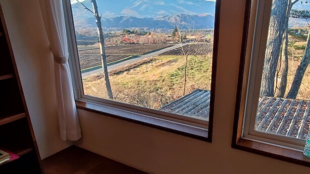 Een kamer met een groot raam met uitzicht op een landelijk gebied met velden en bergen.