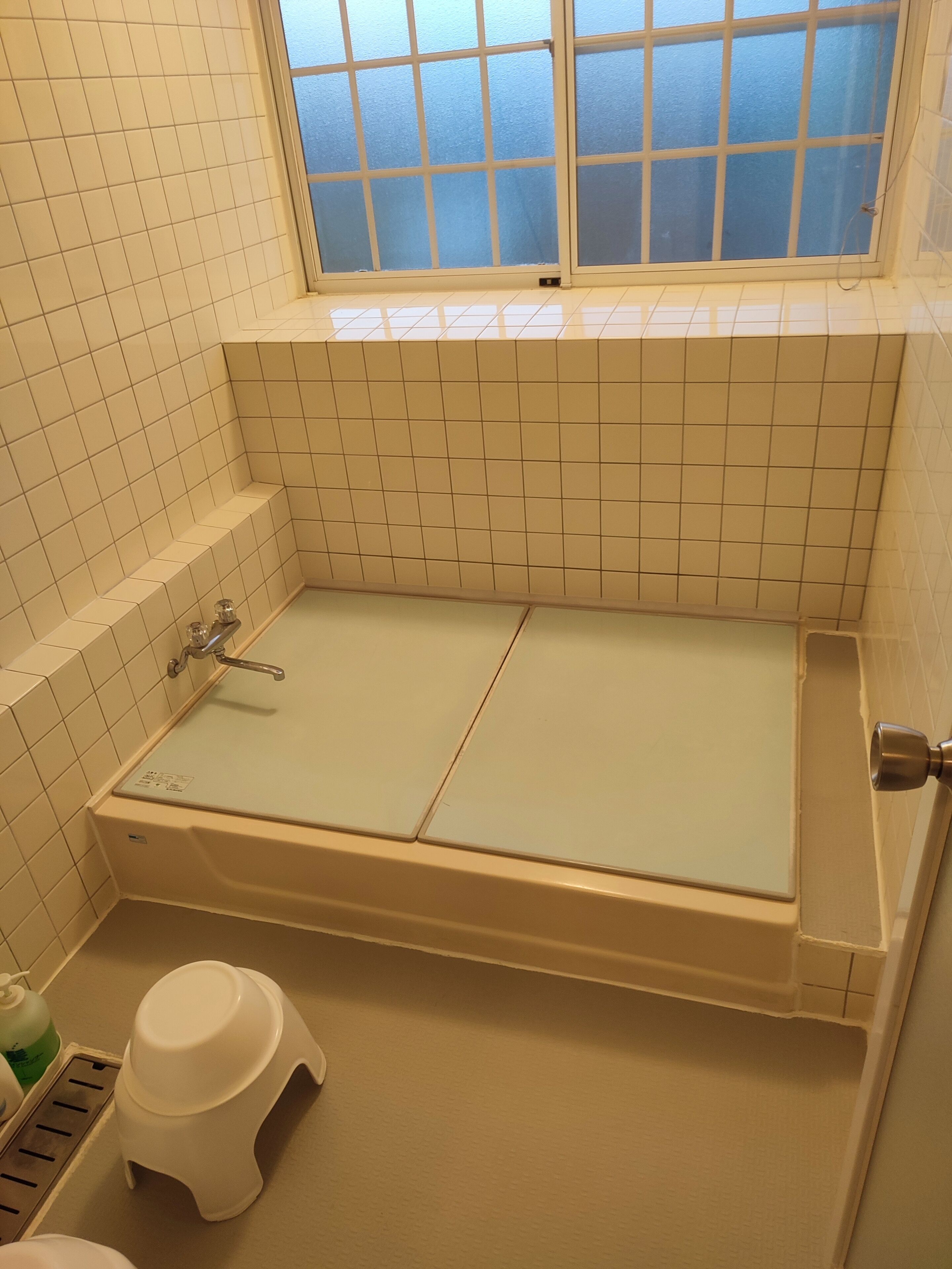 Et lille badeværelse med fliser, badekar, et vindue og et toilet.