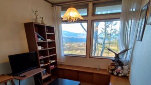 Een knusse woonkamer met een flatscreen-tv, houten planken, een bankje en een groot raam met uitzicht op het landschap.