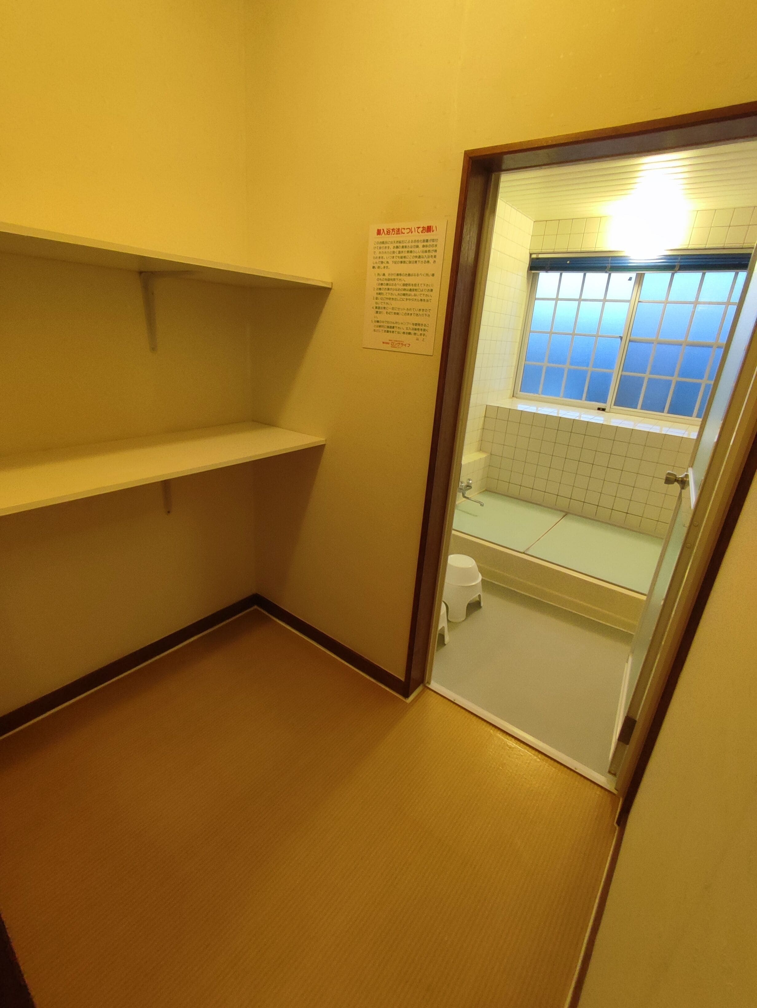 A small bathroom with a toilet, a sink, and a window. There is a sign on the wall with text.