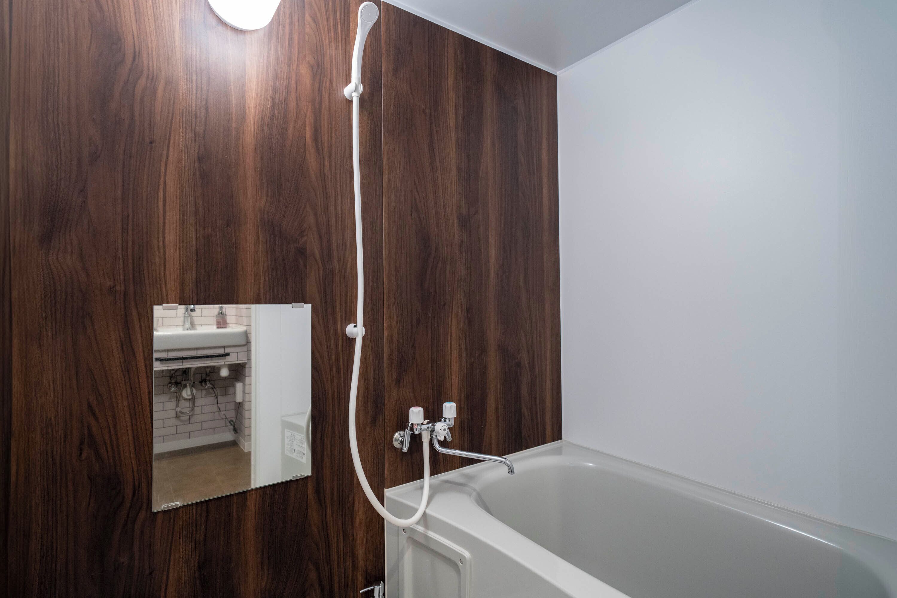 A bathroom with a wooden wall, a white bathtub, and a mirror reflecting the room.