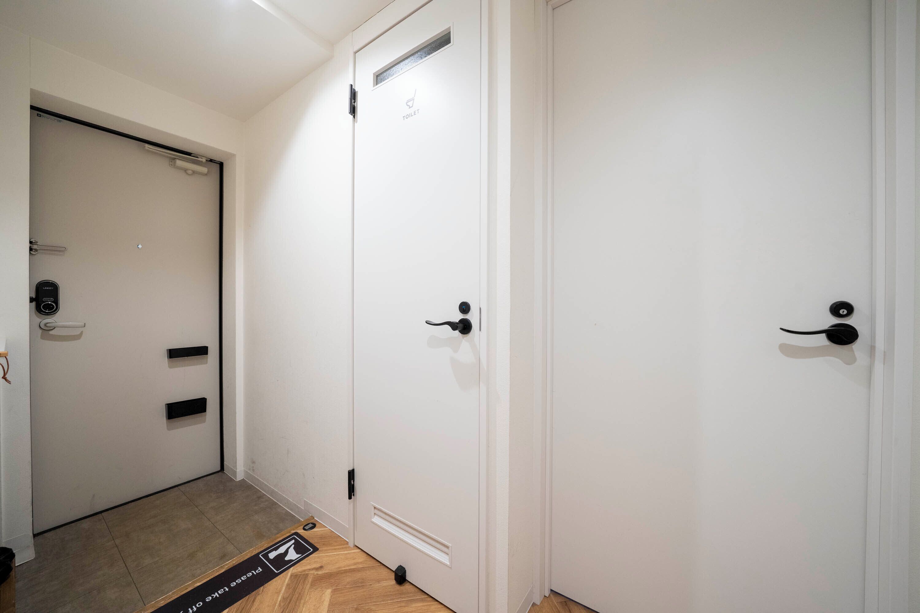 Um corredor com três portas brancas, cada uma com maçaneta preta e uma pequena ventoinha acima da porta.