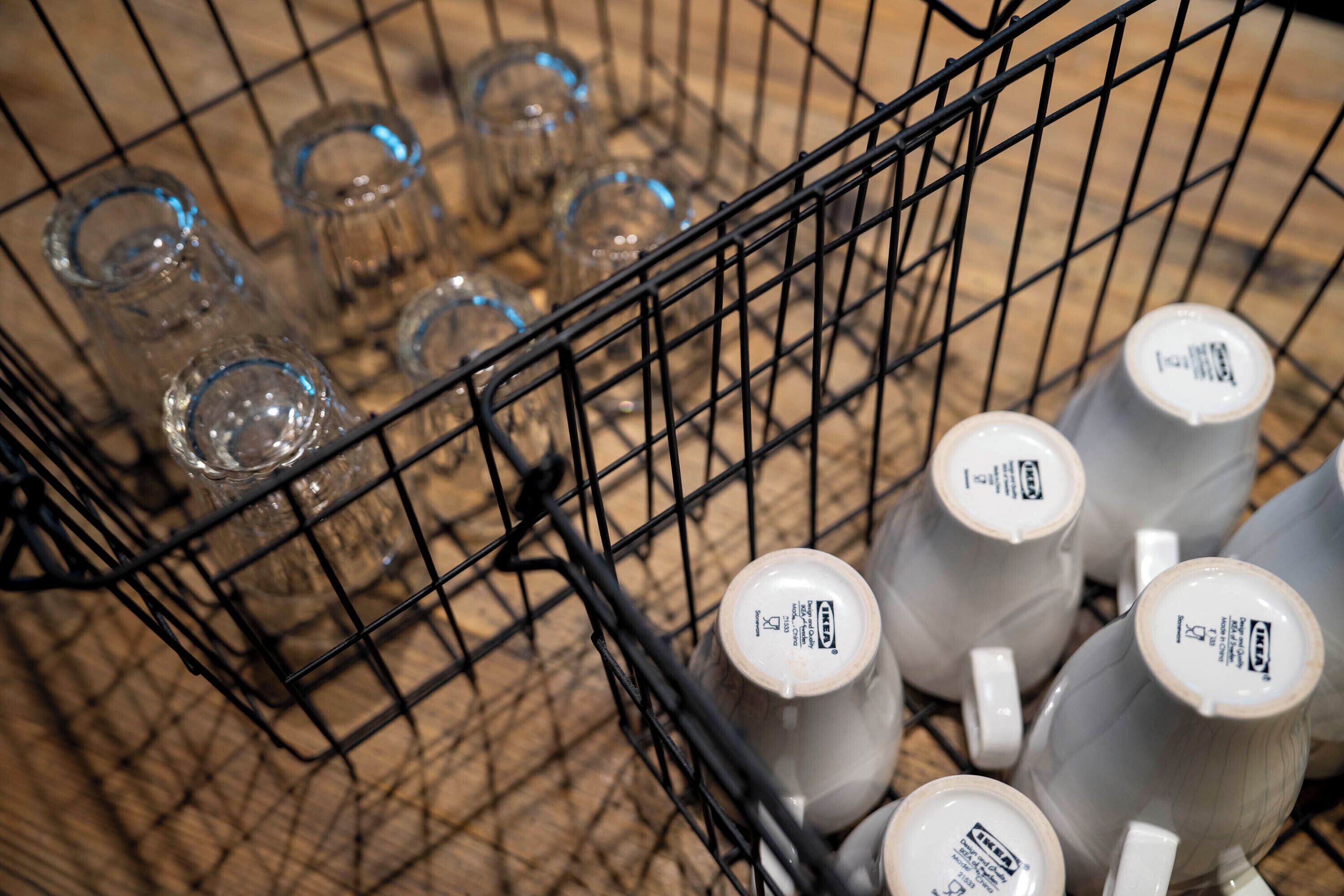 A shopping cart containing clear glassware and white ceramic mugs with lids.