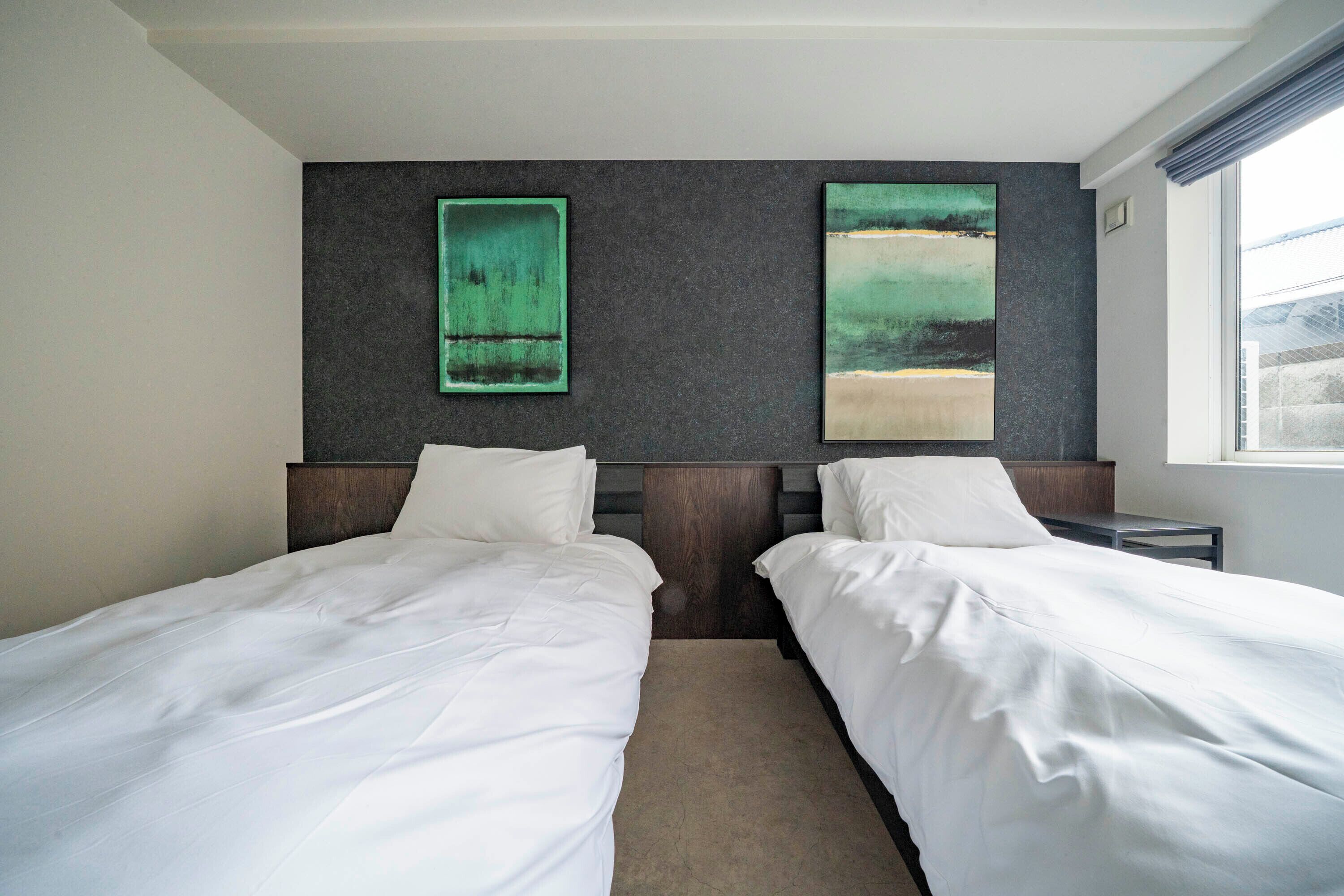 Une chambre d’hôtel avec deux lits, un mur à la texture sombre et deux tableaux.