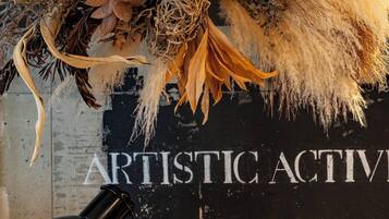 A decorative arrangement with a sign reading "ARTISTIC ACTIVITIES BEAUTIFUL WITH DEAL WITH" in a room with a concrete wall and a hanging lamp.
