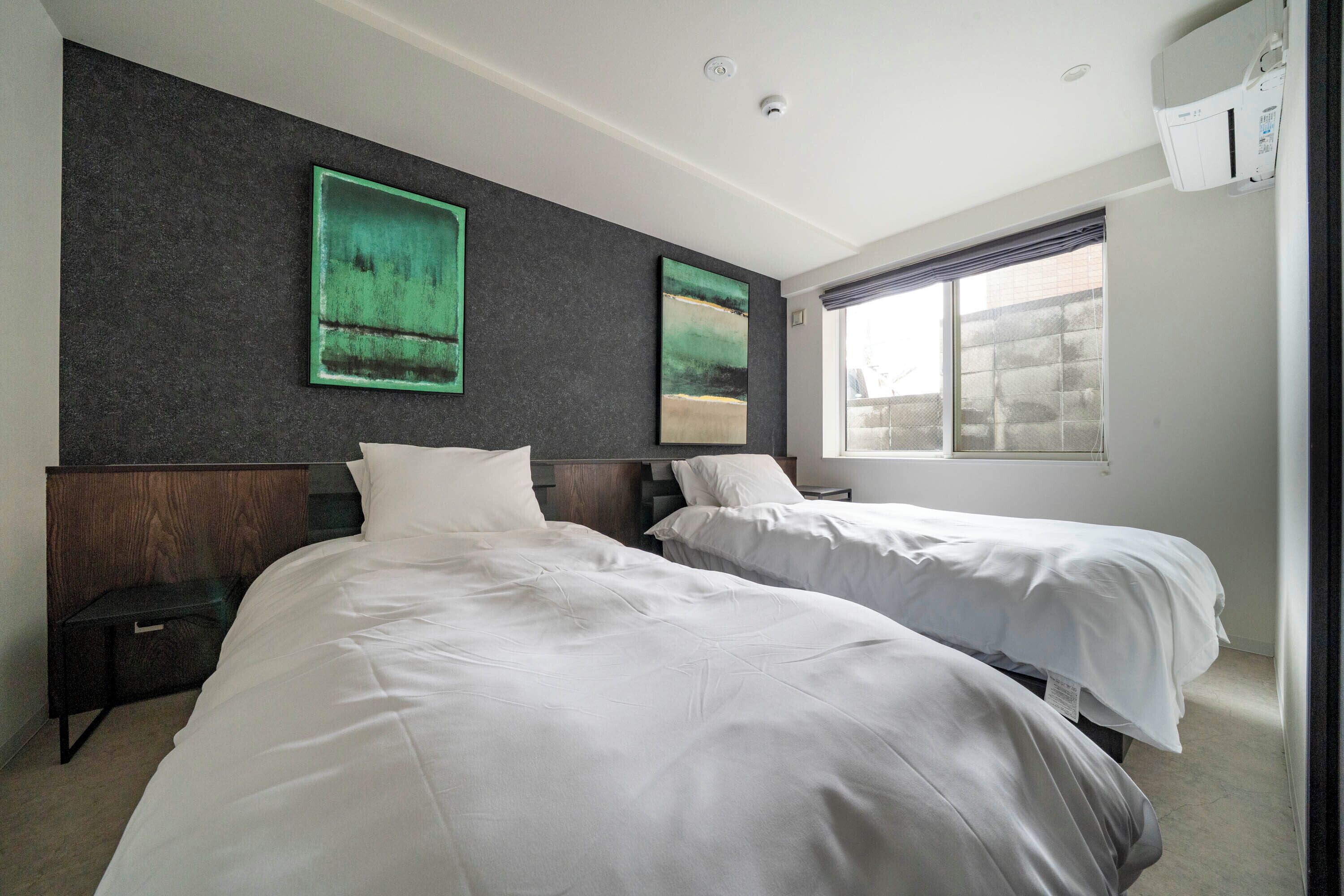 A hotel room with two beds, dark textured walls, and artwork.