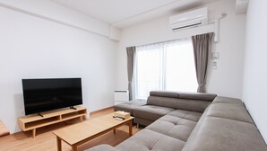 Ein modernes Wohnzimmer mit Flachbildfernseher, einem Holztisch und einem großen grauen Sofa.