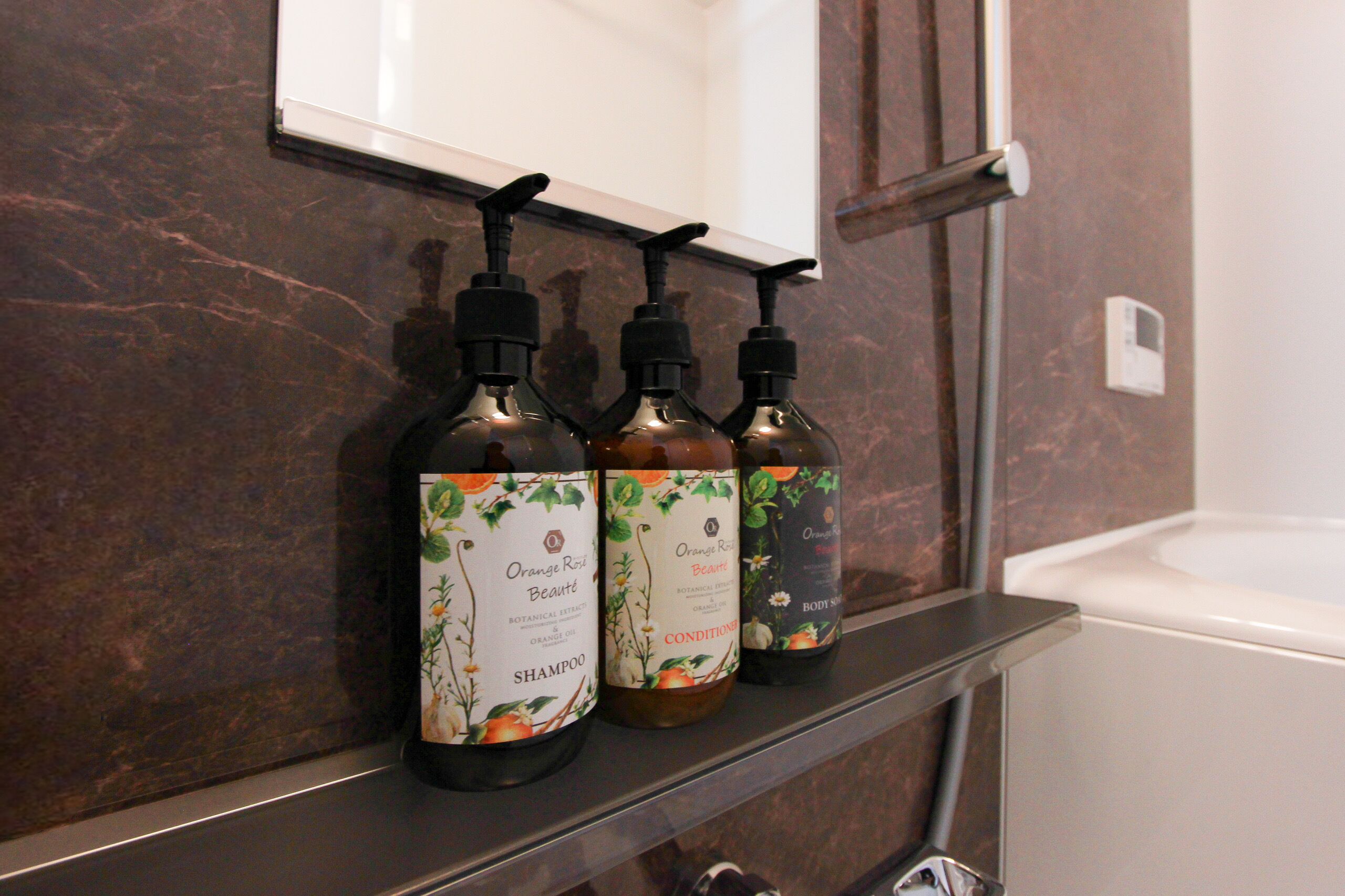 Three bottles of Orange Rose Beauté shampoo on a shelf in a bathroom.