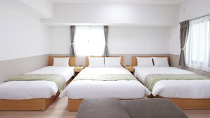 Ein Hotelzimmer mit drei Einzelbetten, einem großen Fenster mit Vorhängen, einer Deckenleuchte und einer kleinen Sitzecke.