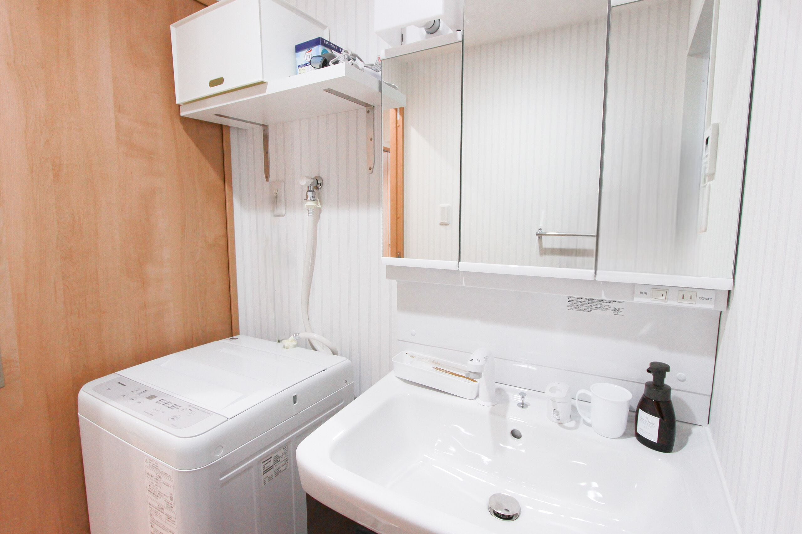 Un bany compacte amb una rentadora blanca, un lavabo i un mirall.