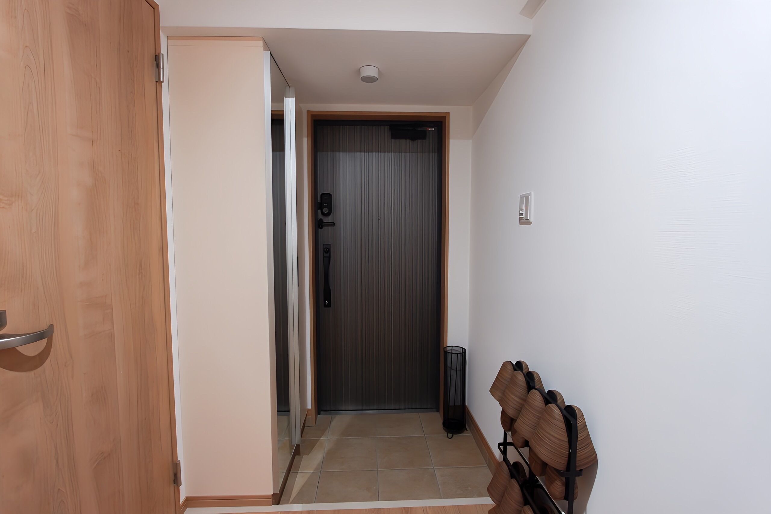 A hallway with a wooden door, a grey door, and a trash bin.