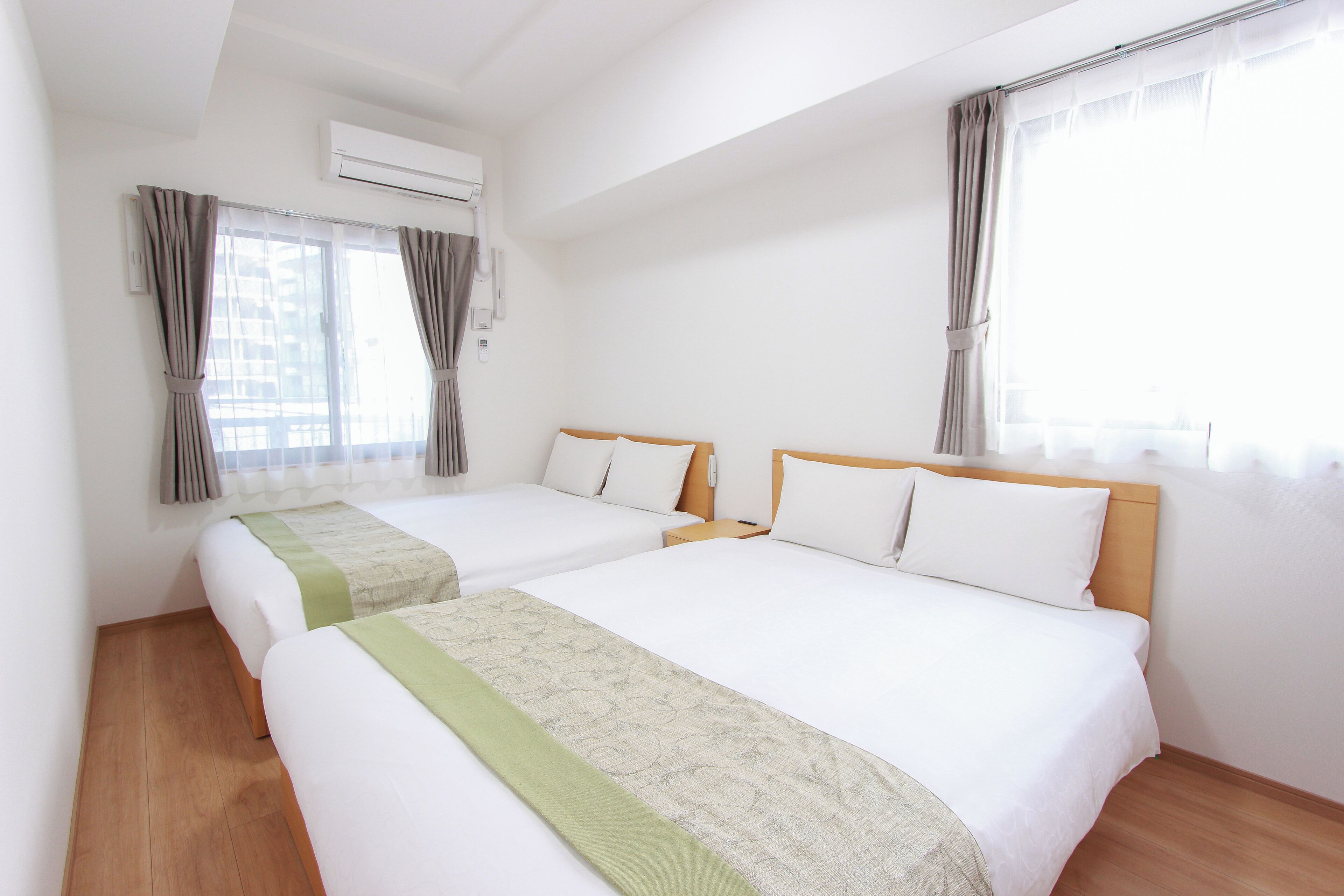 Een hotelkamer met twee bedden, een houten vloer en een airconditioning.