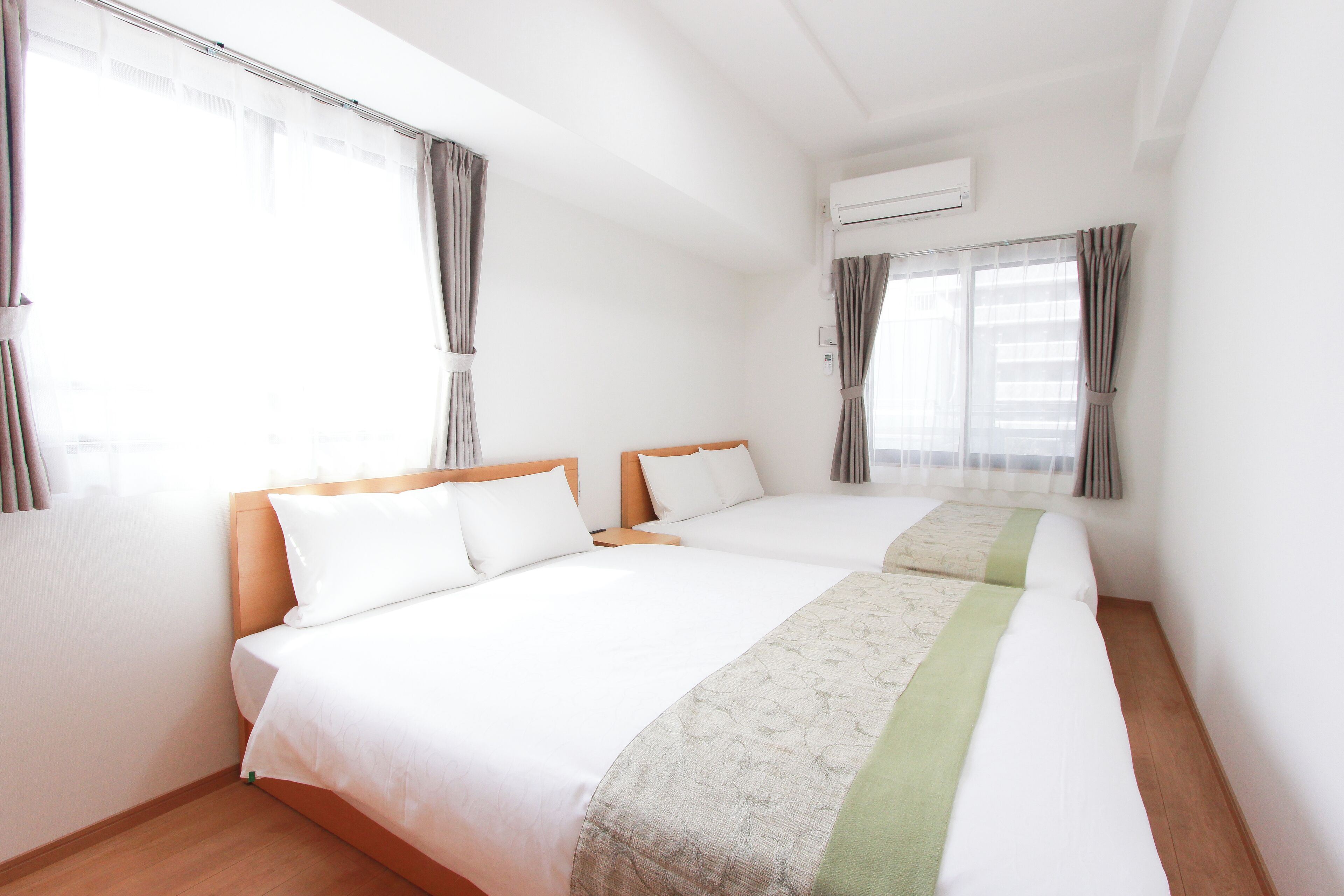 A hotel room with two beds, a wooden headboard, white bedding, and a window with curtains.