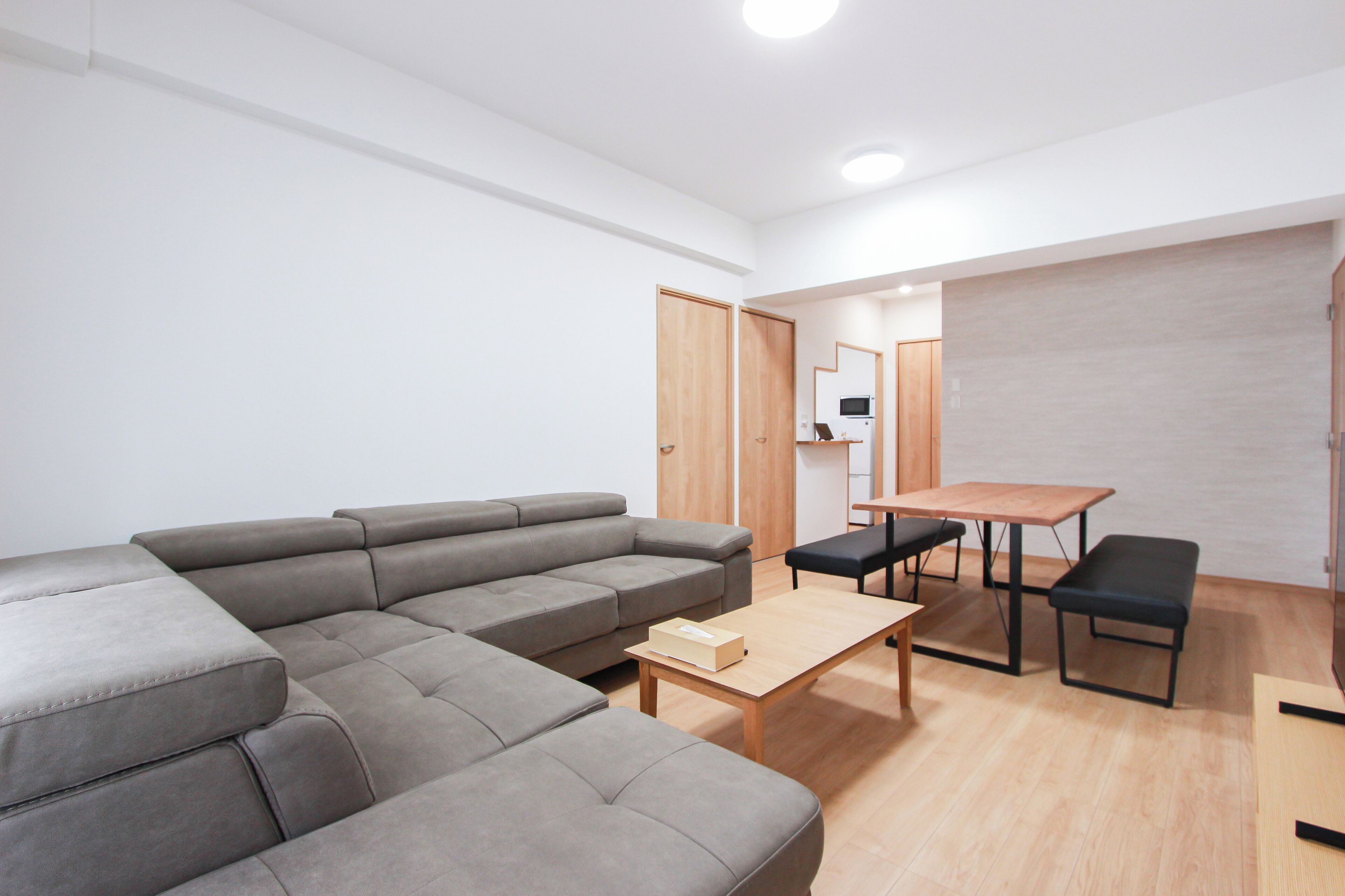 A modern living room with a sectional sofa, a wooden coffee table, and a dining area with a table and benches.