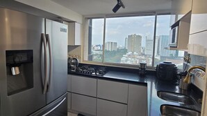 Una cocina moderna con electrodomésticos de acero inoxidable, un amplio ventanal con vistas a la ciudad y un tapete a rayas blanco y negro.