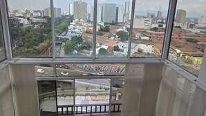 Una habitación con ventanas amplias, vista a un paisaje urbano y dos sillas rosadas.