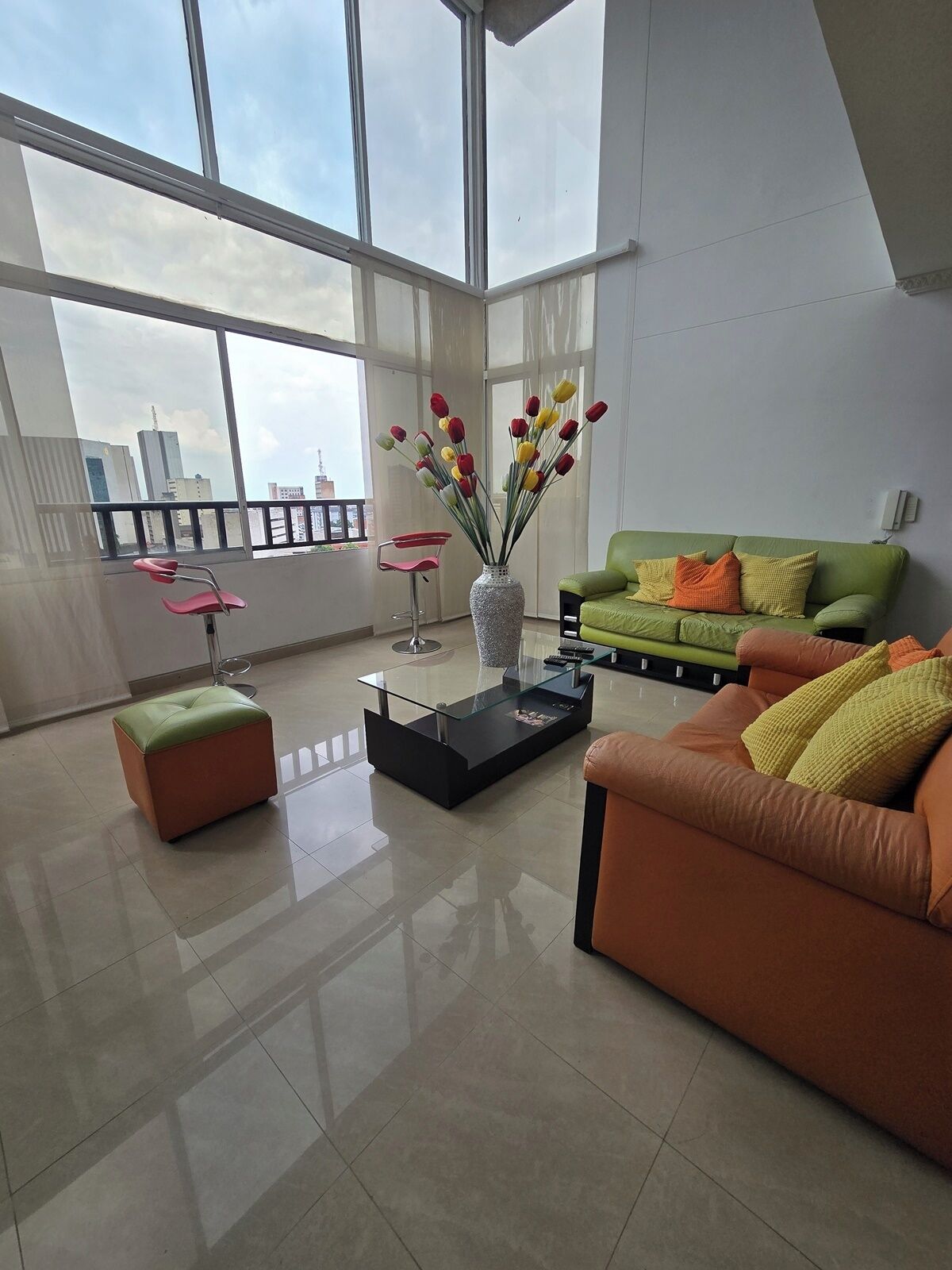 A modern living room with a glass coffee table, a green sofa with orange cushions, and a vase of tulips.