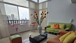 Una sala de estar moderna con una mesa de centro de vidrio, un sofá verde con cojines naranjas y un jarrón con tulipanes.